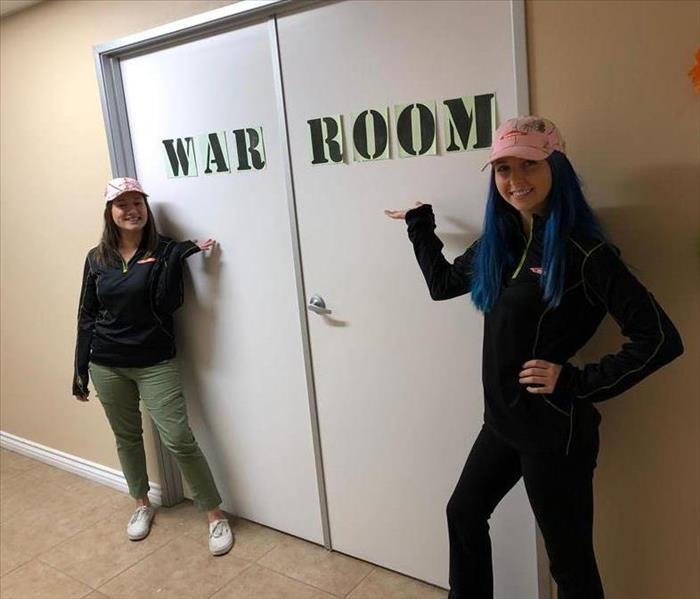two females pointing to doors that say "war room"